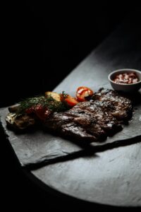 Succulent grilled steak with roasted veggies and sauce on a slate plate.